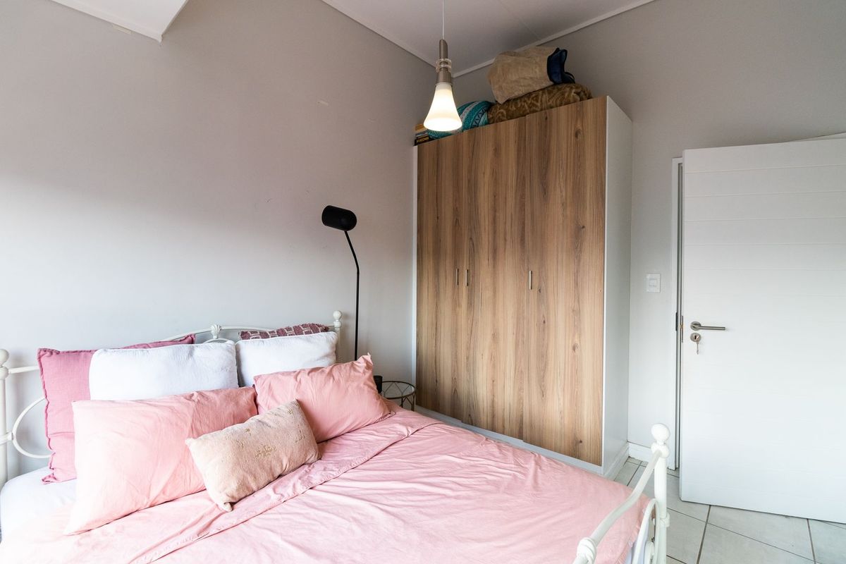 A well-lit bedroom featuring a modern wood-finish built-in wardrobe, neutral wall tones, and tiled flooring.