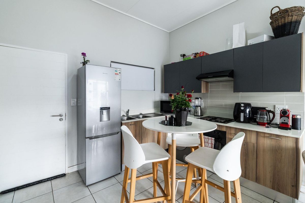 Modern kitchen featuring dark grey upper cabinets, wood-finish lower cabinetry, tiled backsplash, and integrated appliances, providing a functional and contemporary cooking space.
