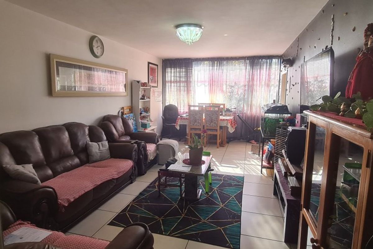 A spacious living room featuring tiled flooring and a large window, providing a functional and well-lit area for relaxation and dining.