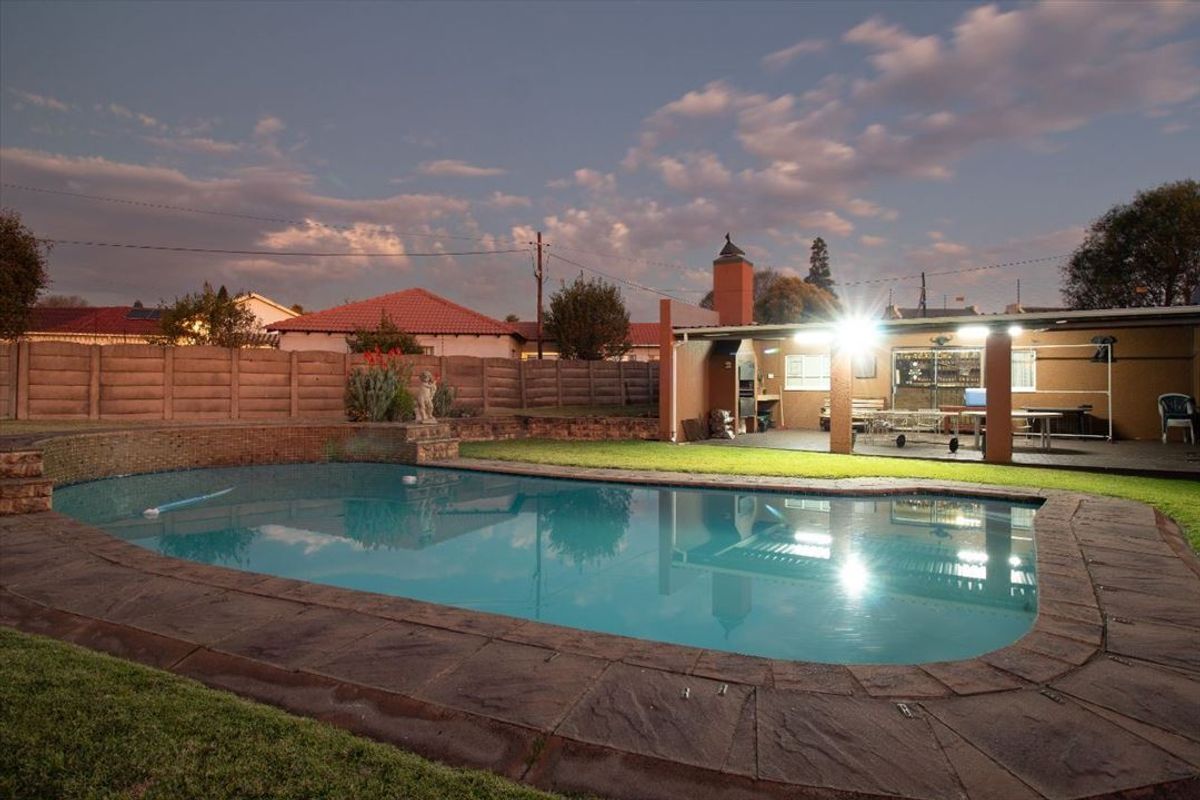 Outdoor entertainment area featuring a swimming pool with stone coping, a covered patio with a built-in braai, and a secure brick boundary wall.