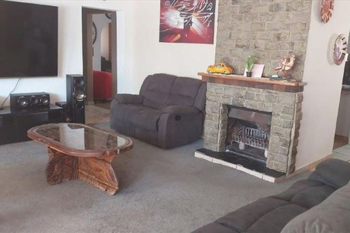 A living room featuring a prominent stone fireplace with a timber mantelpiece and an arched doorway leading to adjacent living spaces.