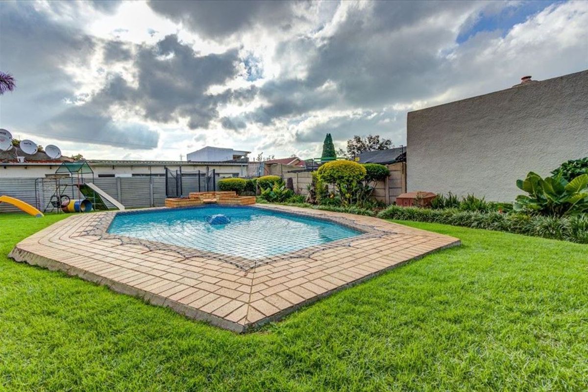 A backyard area featuring a swimming pool with brick coping, surrounded by a well-maintained lawn and perimeter boundary walls.