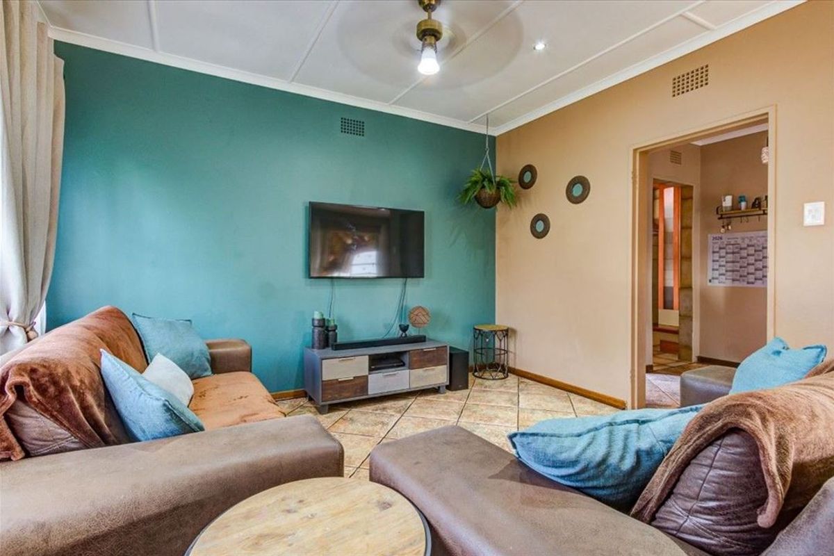 A comfortable living room featuring tiled flooring, a ceiling fan, and a dual-tone wall finish, providing a functional space for relaxation.