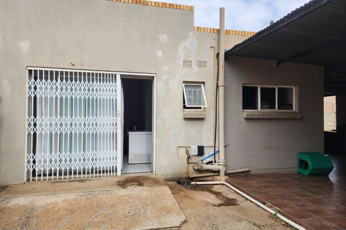 Rear exterior view of the property featuring a covered patio area, security gate, and access to the interior.
