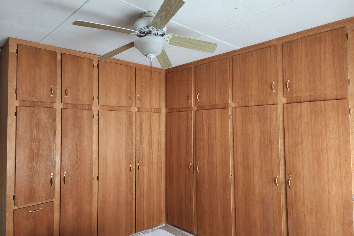 A bedroom featuring extensive floor-to-ceiling built-in wooden cabinetry and a ceiling fan, showing signs of wear on the ceiling.