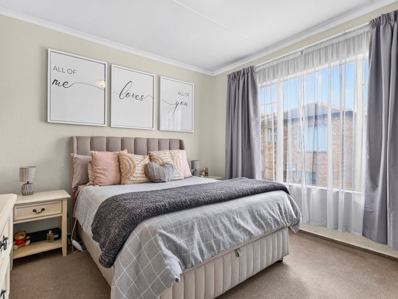 A well-maintained bedroom featuring neutral wall tones, carpeted flooring, and large windows with layered curtains, providing a comfortable and bright living space.