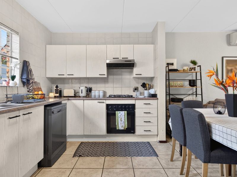An open-plan kitchen featuring light-toned cabinetry, a gas hob, built-in oven, and tiled flooring, seamlessly flowing into the adjacent dining area.