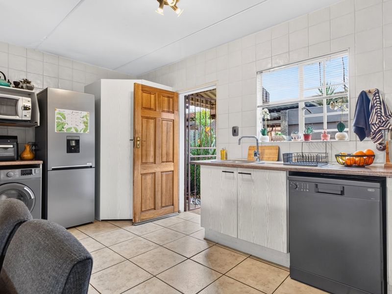 Functional kitchen featuring tiled walls and flooring, laminate countertops, stainless steel sink, and direct access to an outdoor area.