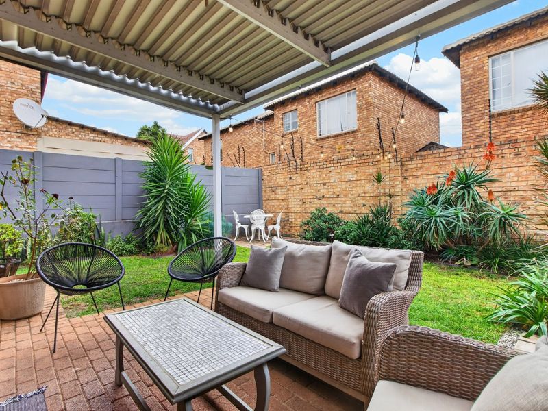 A covered patio area featuring brick paving and a corrugated metal roof, overlooking a private garden with established landscaping and brick boundary walls.