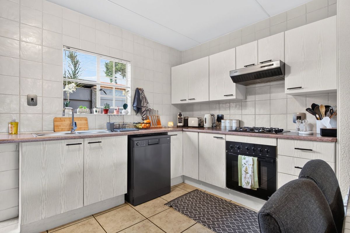 Functional kitchen featuring light wood-grain cabinetry, laminate countertops, gas hob, built-in oven, extractor fan, and tiled finishes throughout.
