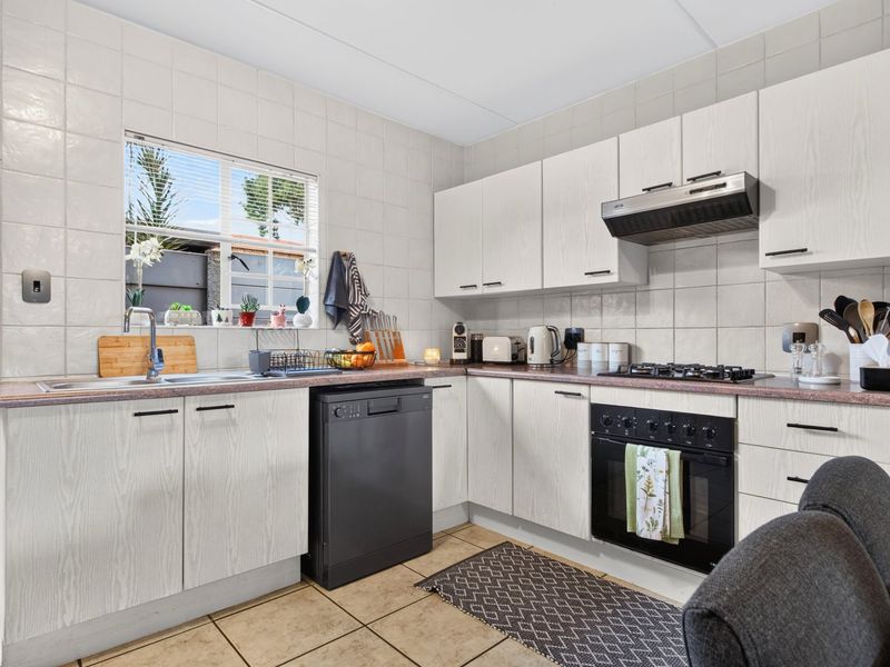 Functional kitchen featuring light wood-grain cabinetry, laminate countertops, gas hob, built-in oven, extractor fan, and tiled finishes throughout.