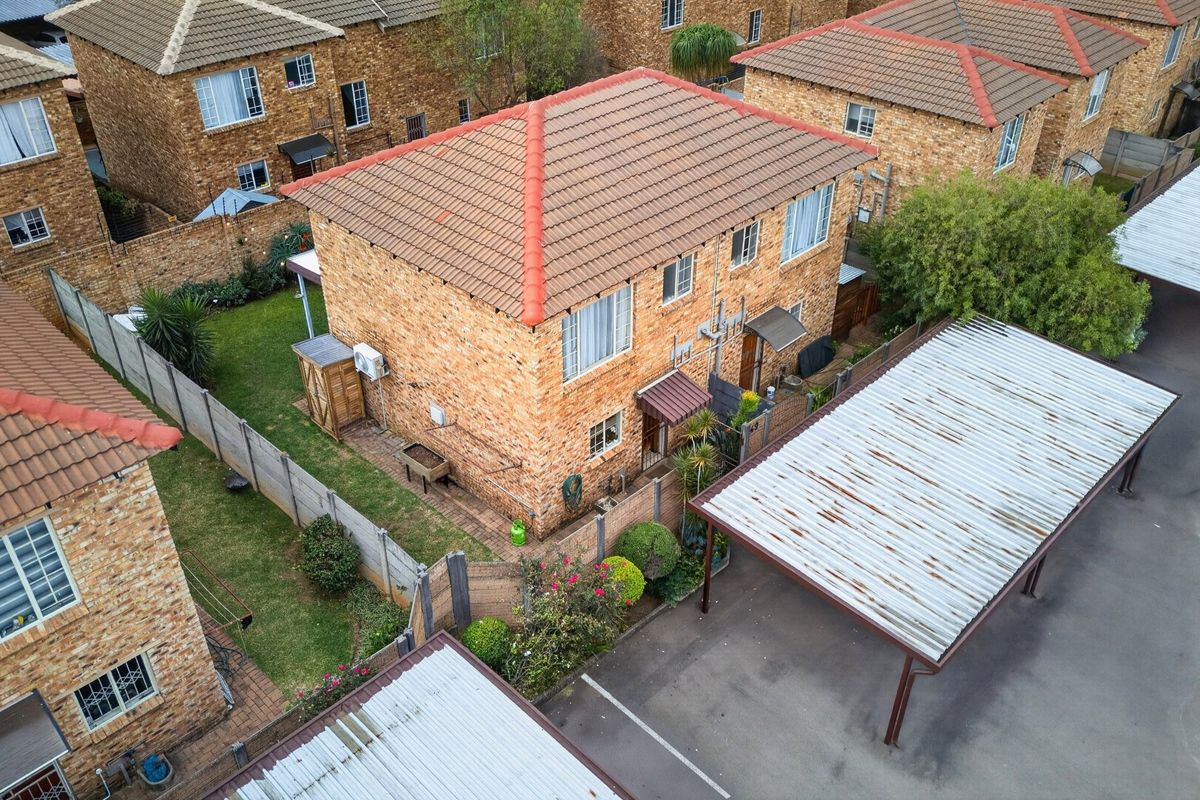 Aerial view of a facebrick townhouse complex featuring a tiled roof, private garden space, and a dedicated carport with corrugated metal roofing.