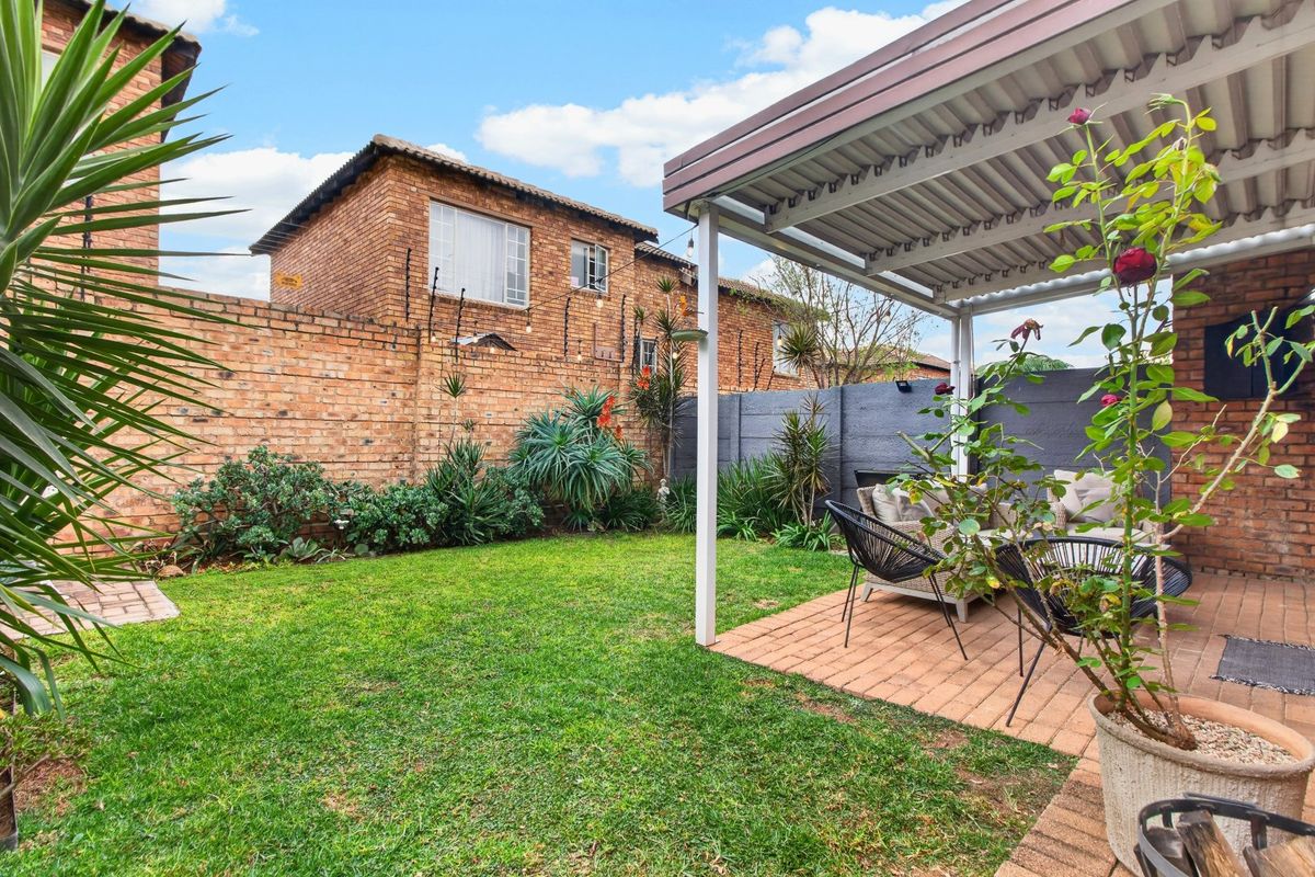 A private rear garden featuring a covered patio area with paved flooring, established lawn, and secure brick boundary walls.