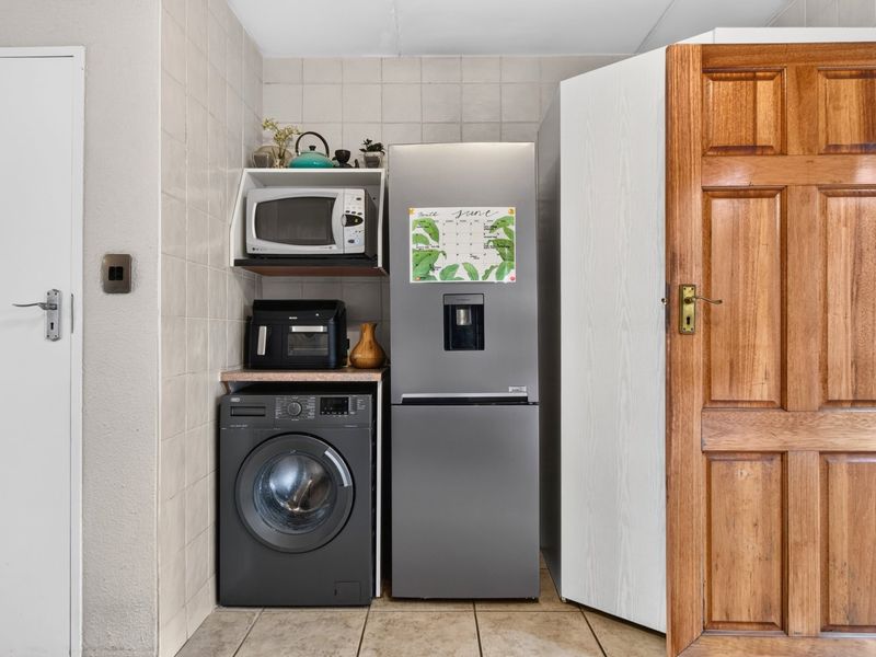 A functional laundry area featuring tiled walls and flooring, with dedicated space for appliances and built-in shelving.