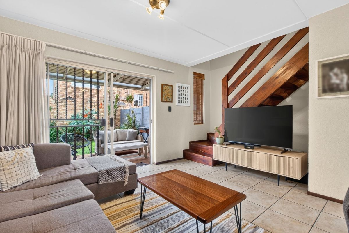 Open-plan living area featuring tiled floors, a wooden staircase, and large sliding glass doors providing direct access to the rear patio and garden.