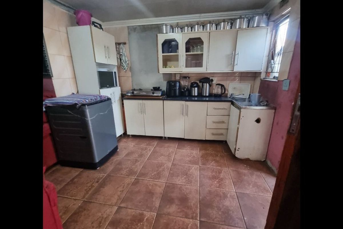 A functional kitchen featuring tiled flooring, built-in cabinetry, and a tiled splashback, currently showing signs of wear and requiring cosmetic updates.