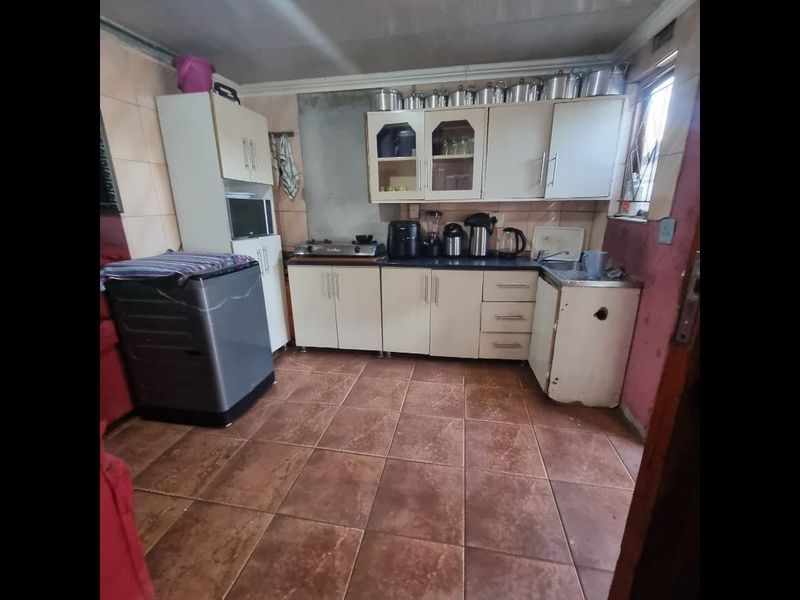 A functional kitchen featuring tiled flooring, built-in cabinetry, and a tiled splashback, currently showing signs of wear and requiring cosmetic updates.