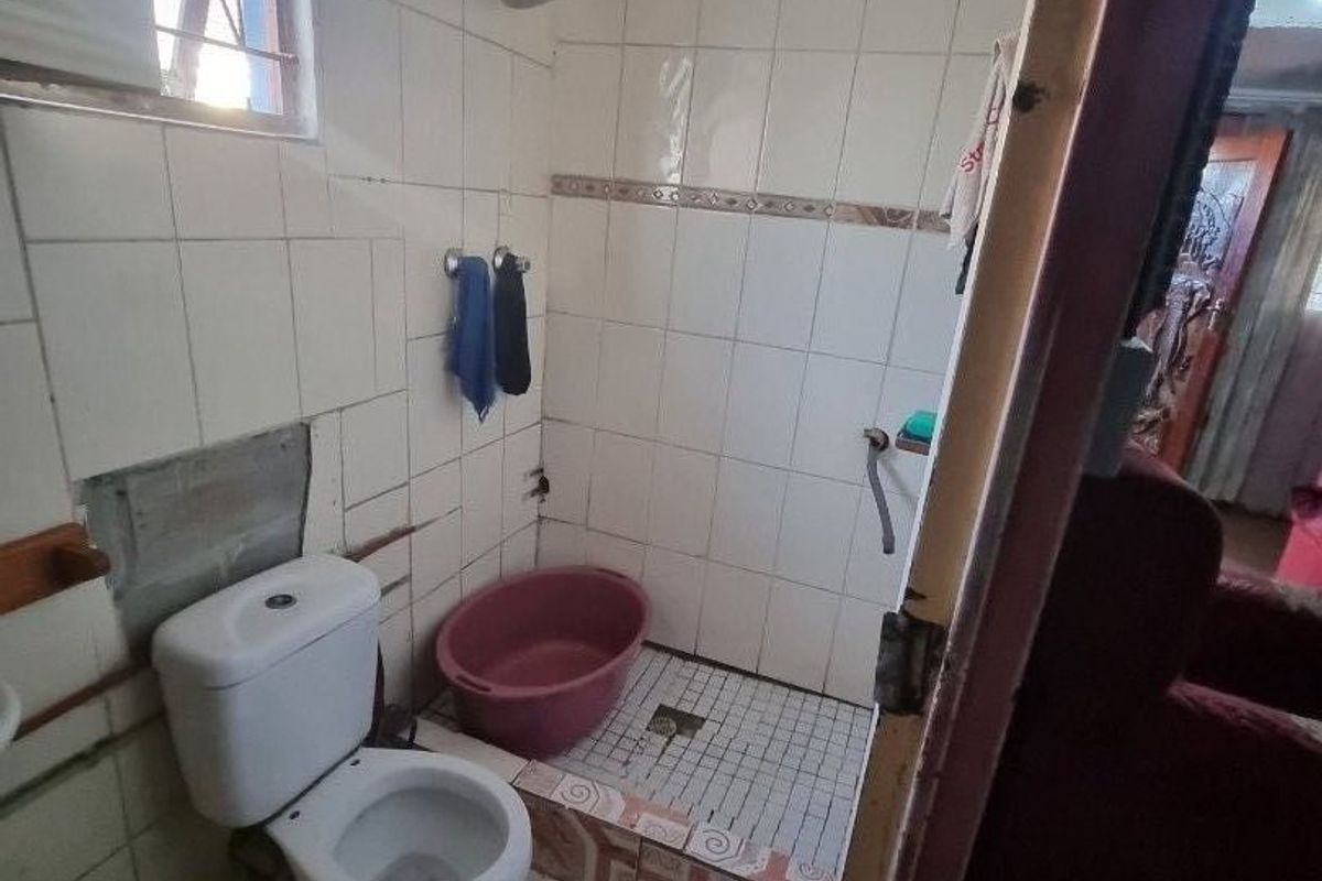 A small bathroom featuring a toilet and a walk-in shower area with tiled finishes, currently requiring maintenance and cosmetic repairs to the wall tiling.