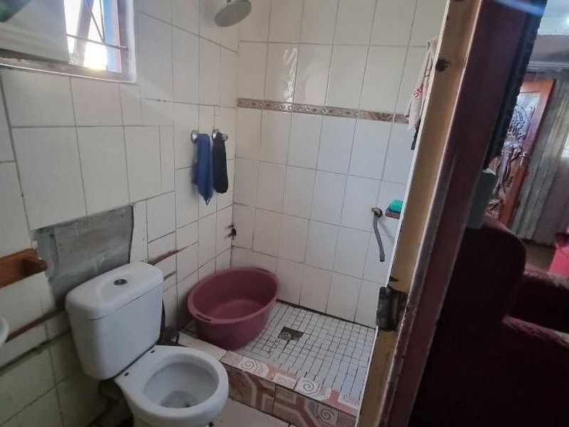 A small bathroom featuring a toilet and a walk-in shower area with tiled finishes, currently requiring maintenance and cosmetic repairs to the wall tiling.