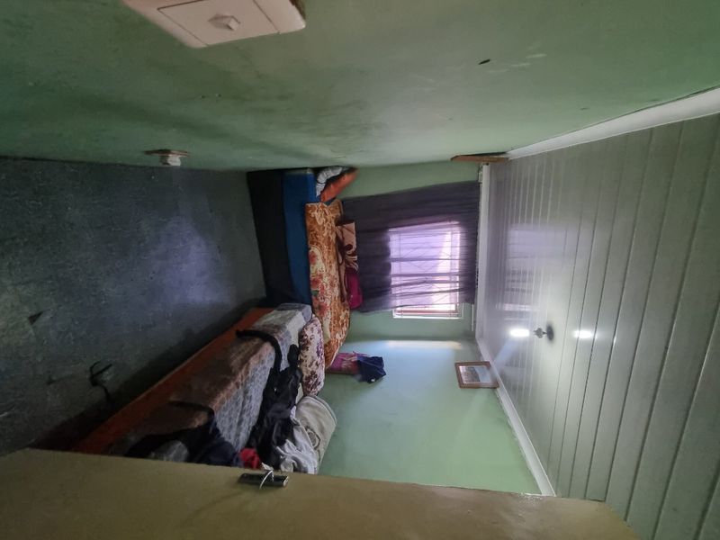 A bedroom featuring green painted walls and plastic ceiling panels, equipped with a window fitted with security bars.