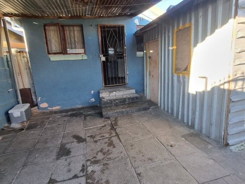 Rear exterior area featuring a paved patio, corrugated iron roofing, and metal wall cladding, showing significant signs of weathering and wear.