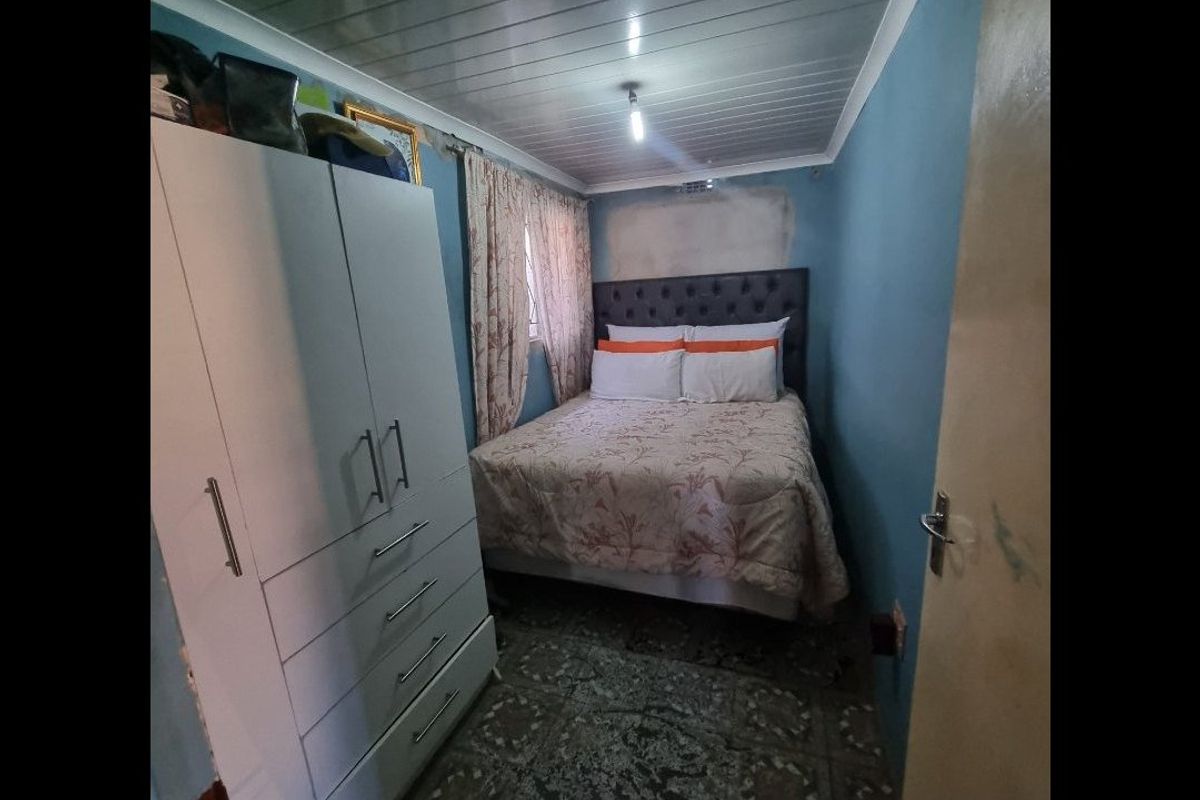A compact bedroom featuring tiled flooring and a panelled ceiling, currently requiring wall repairs and cosmetic updates to improve the overall finish.