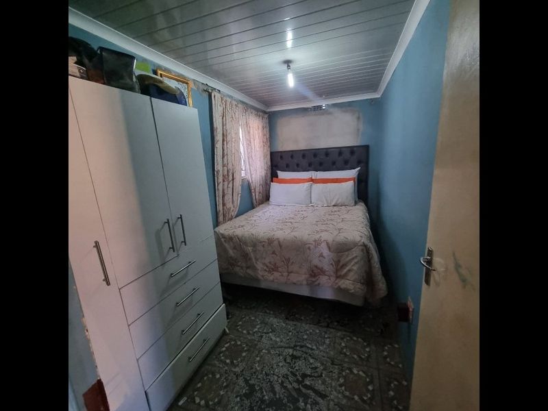 A compact bedroom featuring tiled flooring and a panelled ceiling, currently requiring wall repairs and cosmetic updates to improve the overall finish.