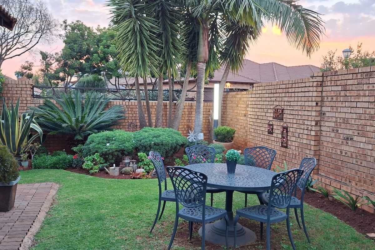 A well-maintained rear garden featuring a brick boundary wall, established palm trees, and a paved walkway area.