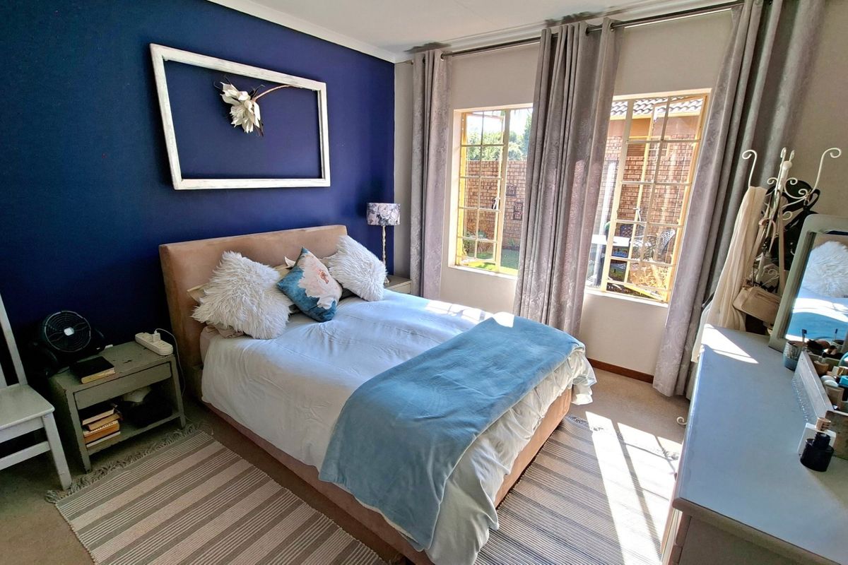 A bedroom featuring a bold blue accent wall, carpeted flooring, and natural light provided by steel-framed windows overlooking the exterior.