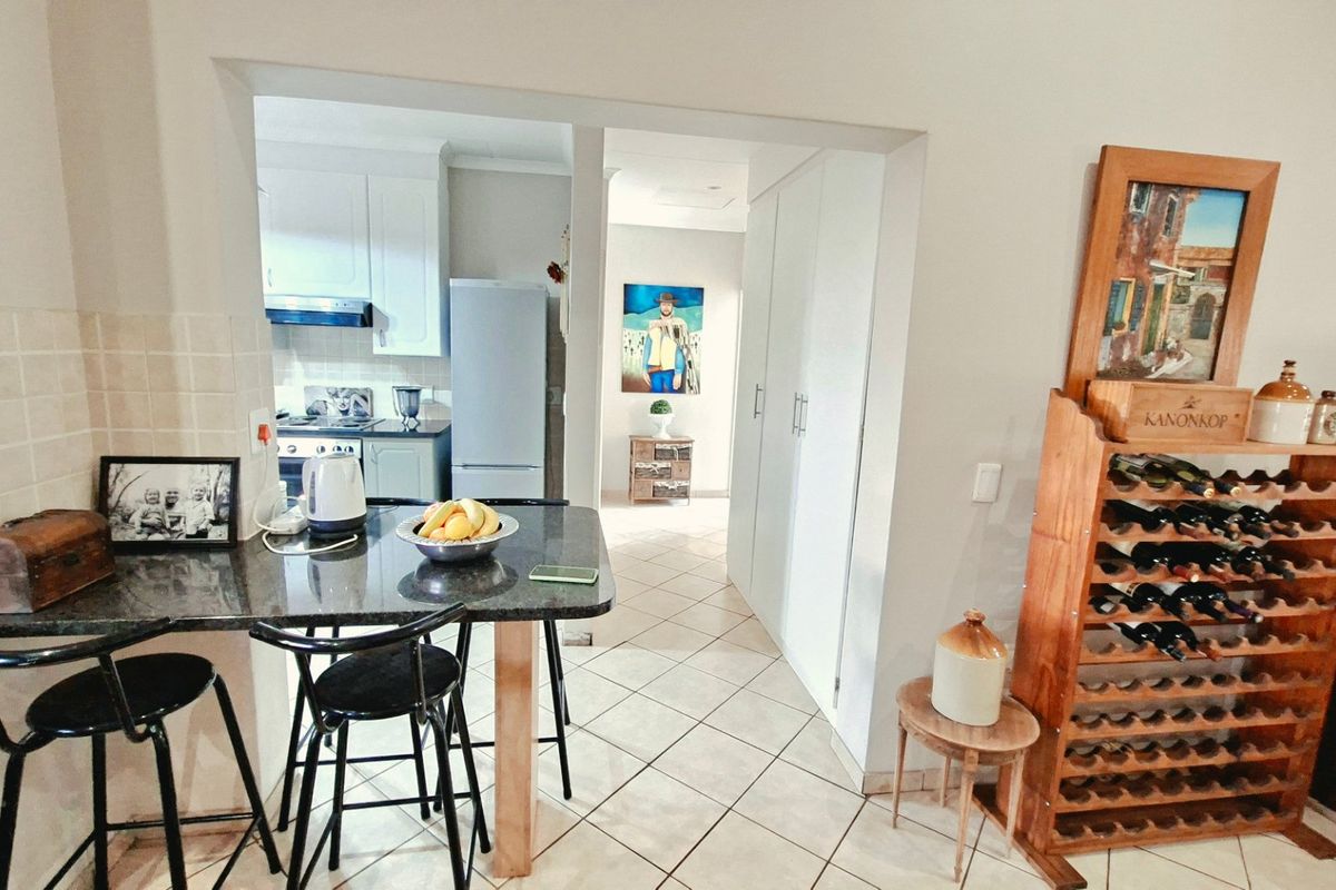 A functional kitchen area featuring granite countertops, ample built-in cabinetry, and tiled flooring, with a breakfast bar and adjacent hallway access.