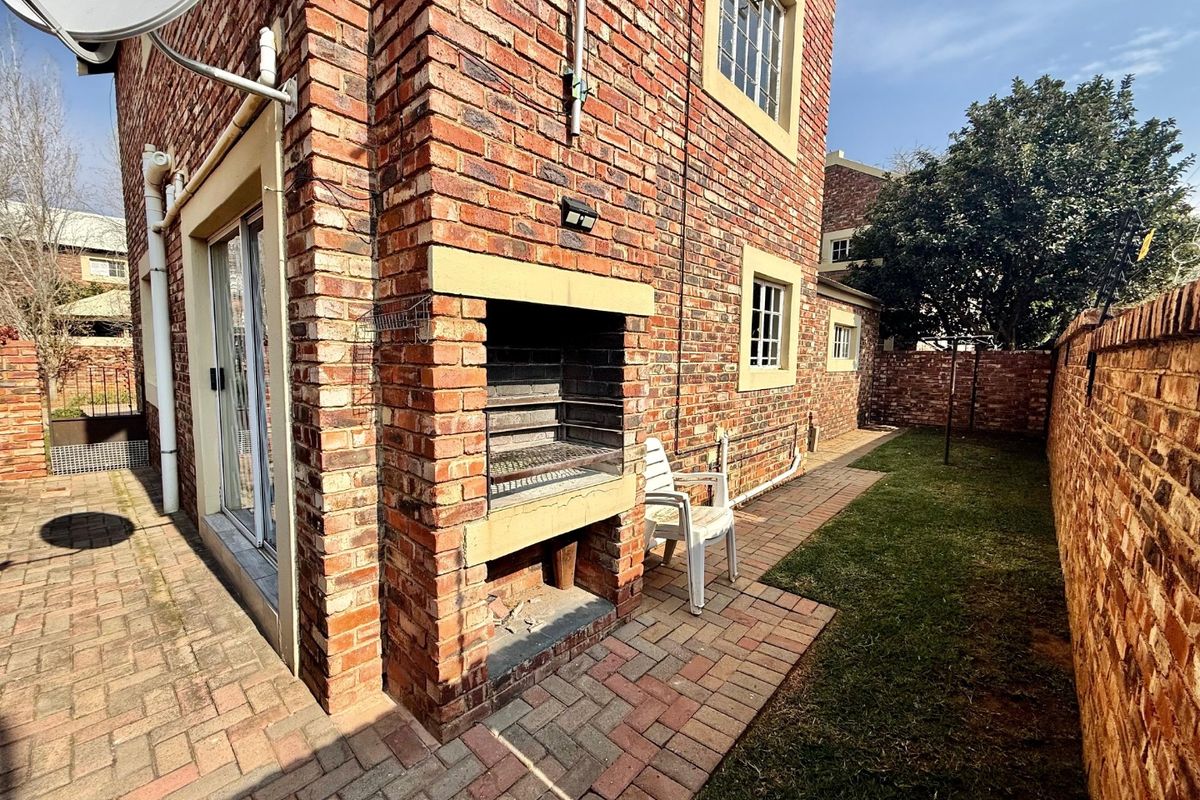 Rear exterior view of the townhouse featuring a paved patio area with a built-in brick braai and a small private garden.