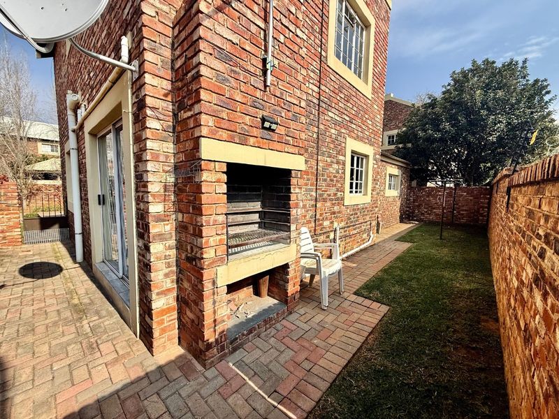 Rear exterior view of the townhouse featuring a paved patio area with a built-in brick braai and a small private garden.