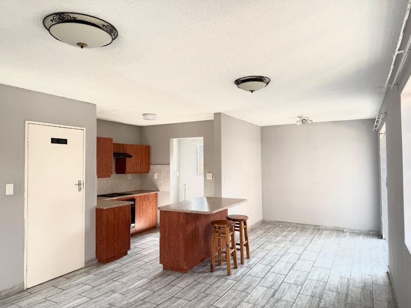 Open plan kitchen and living area featuring wood-tone cabinetry, a central kitchen island, and modern tiled flooring throughout the space.