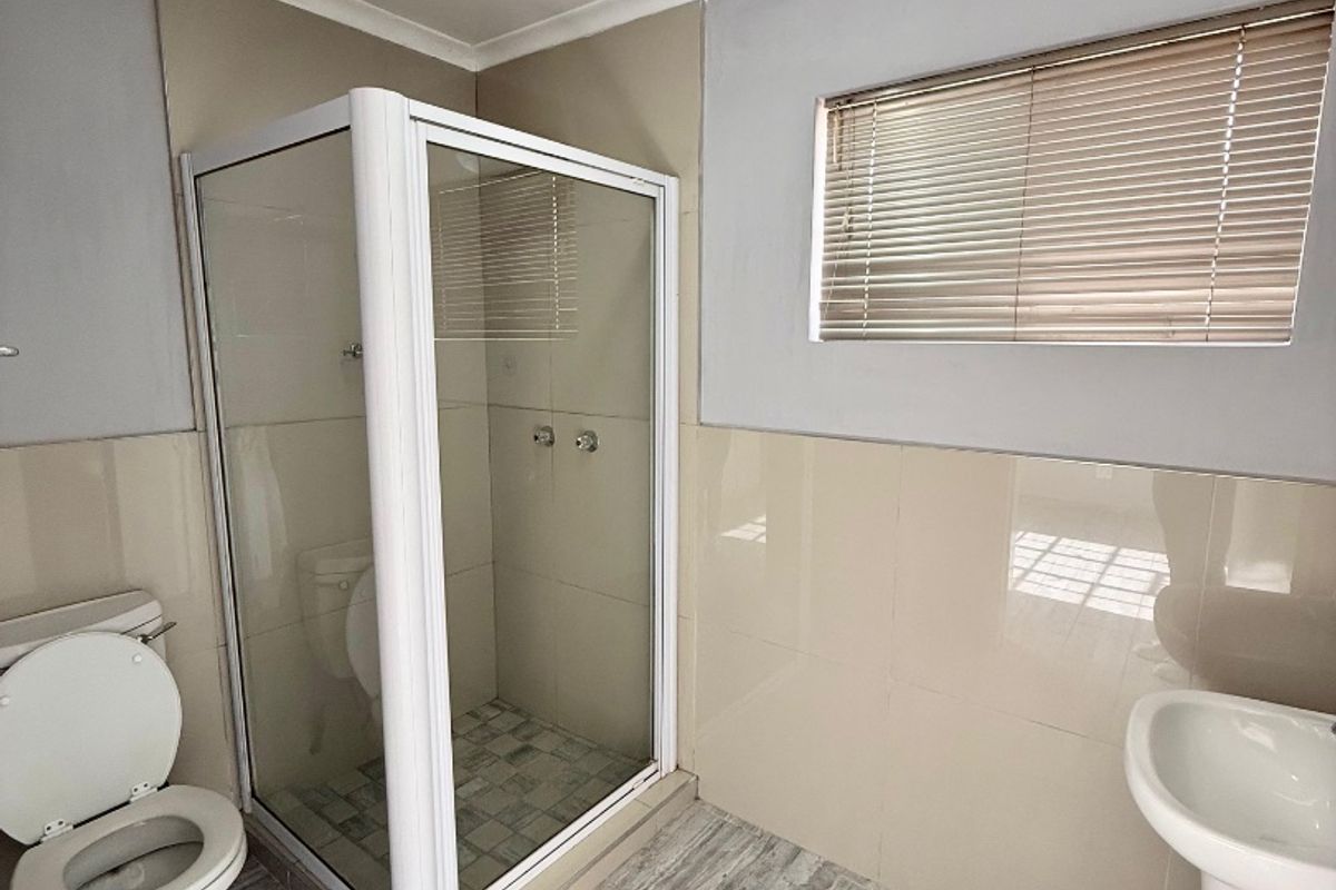 A clean and functional bathroom featuring a glass shower enclosure, pedestal basin, toilet, and neutral wall and floor tiling.