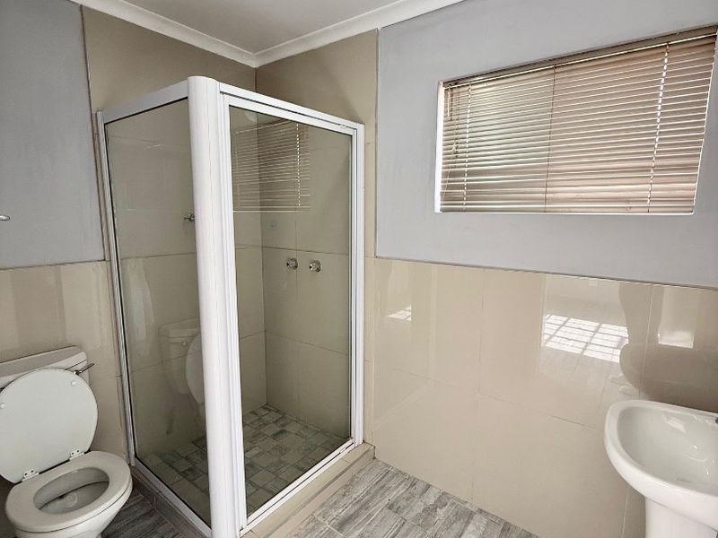 A clean and functional bathroom featuring a glass shower enclosure, pedestal basin, toilet, and neutral wall and floor tiling.