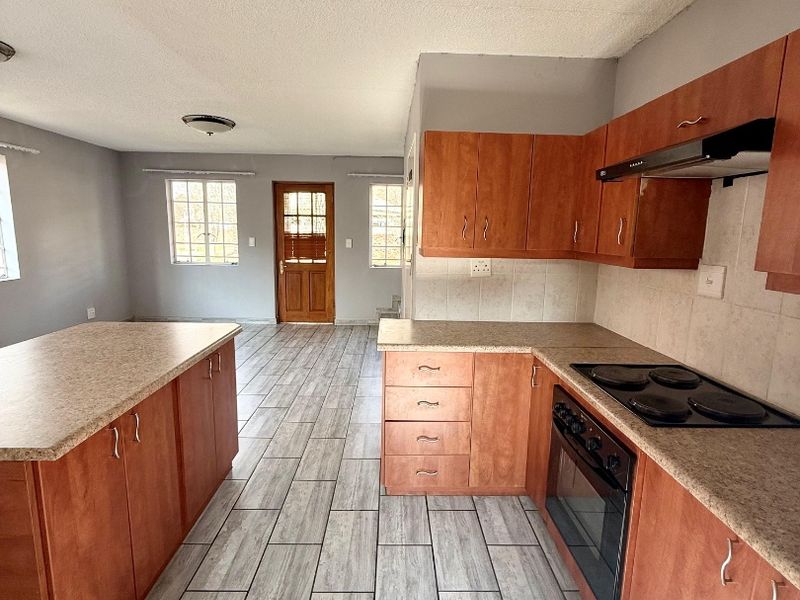 Open-plan kitchen and living area featuring wood-finish cabinetry, laminate countertops, built-in cooking appliances, and modern tiled flooring throughout.