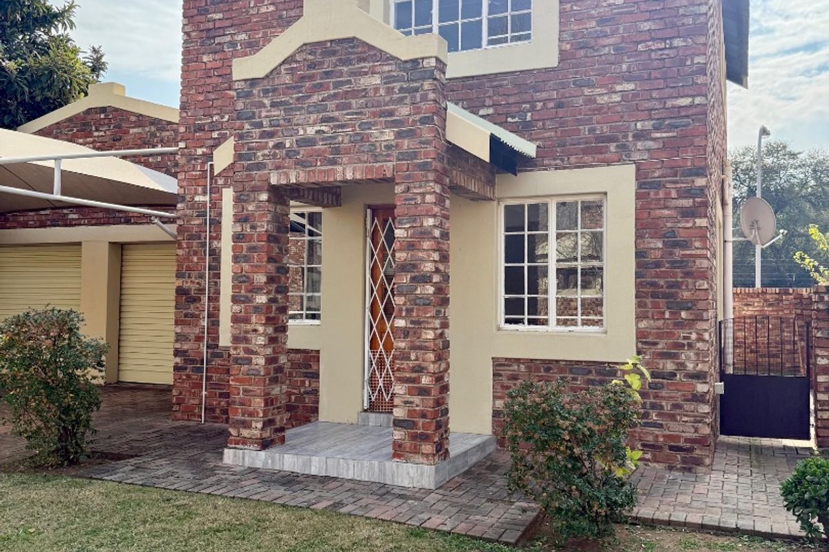 Front elevation of a double-story facebrick townhouse featuring a covered entrance, paved driveway, and attached double garage with carport.