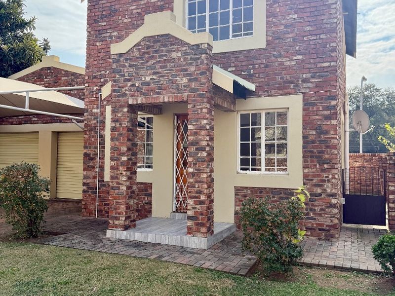 Front elevation of a double-story facebrick townhouse featuring a covered entrance, paved driveway, and attached double garage with carport.