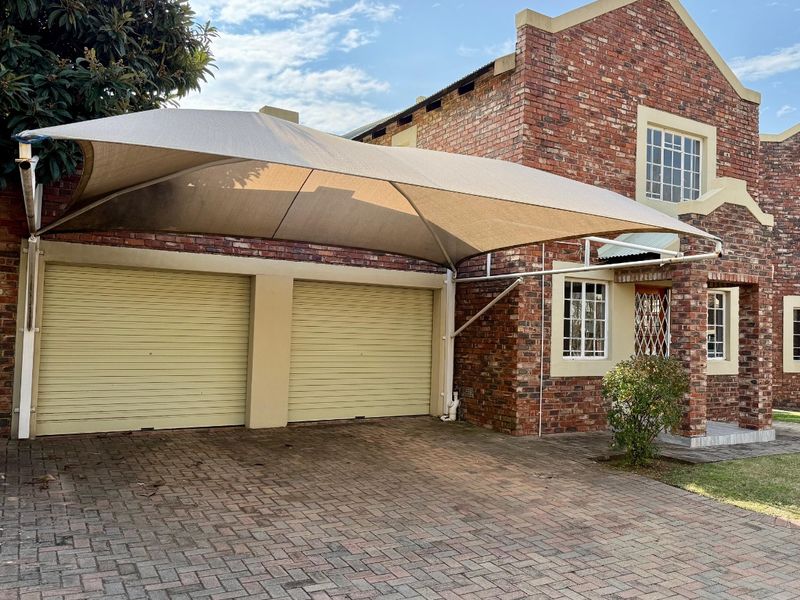 Front elevation of a facebrick townhouse featuring a double garage with roll-up doors, a shade sail carport, and a paved driveway.