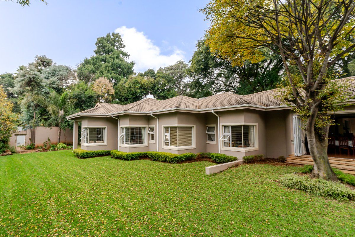 Rear view of the house featuring a well-maintained lawn, mature trees, and multiple bay windows with a tiled roof.