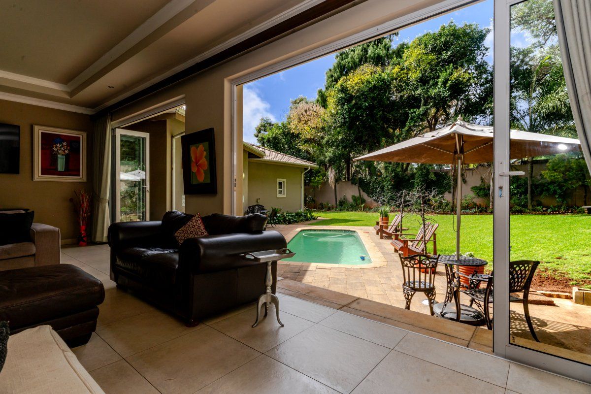 Spacious living area featuring large sliding glass doors that open onto a paved patio, swimming pool, and landscaped garden.