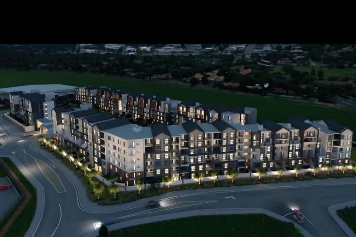 An aerial perspective of a modern multi-story apartment complex development, showcasing the building architecture, layout, and surrounding street infrastructure.