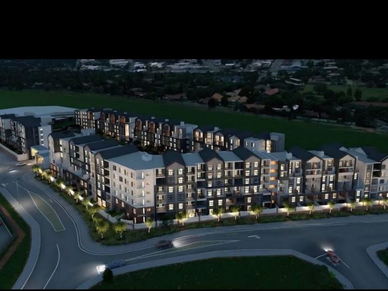An aerial perspective of a modern multi-story apartment complex development, showcasing the building architecture, layout, and surrounding street infrastructure.