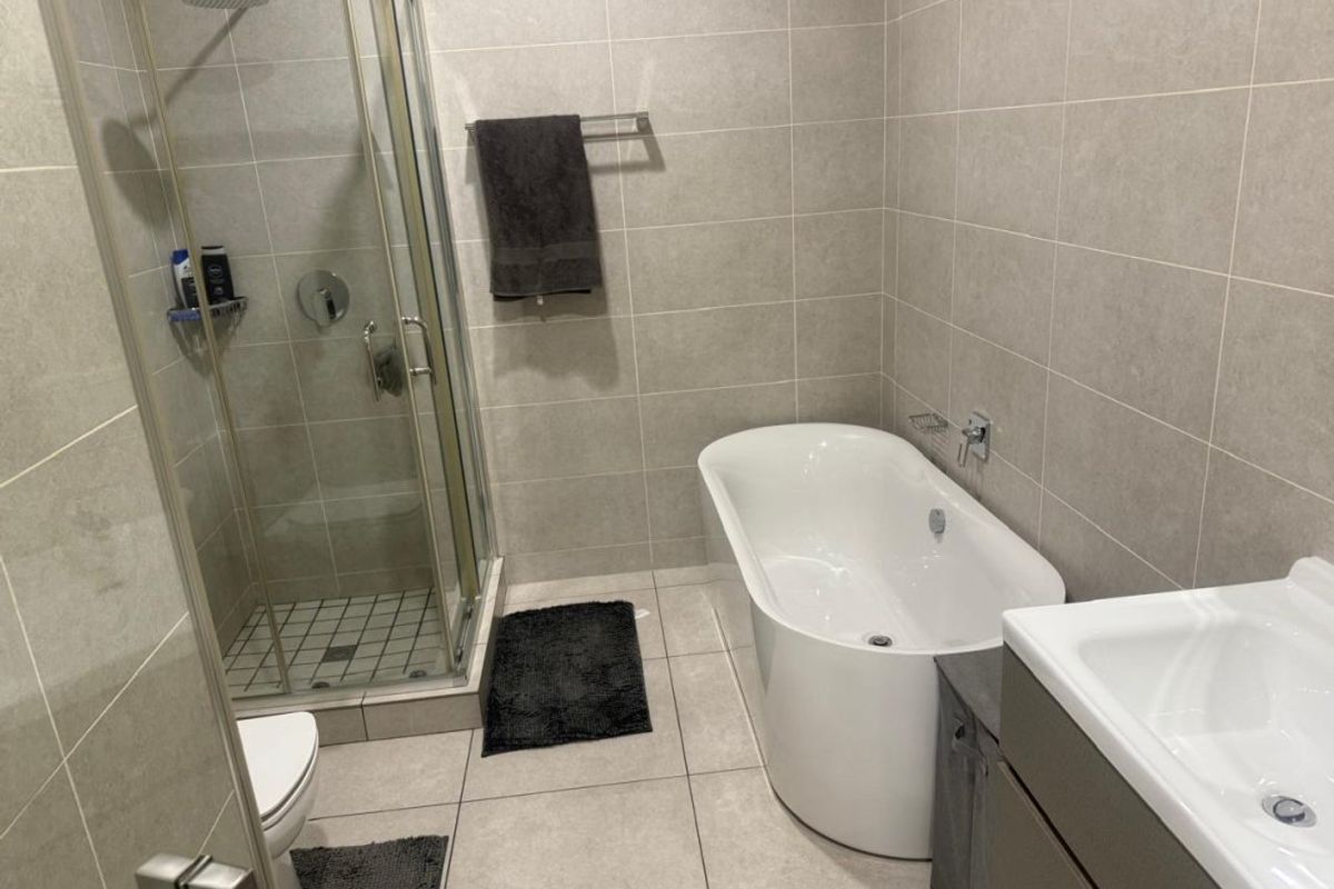 Modern bathroom featuring a freestanding bathtub, separate glass-enclosed shower, and a vanity unit with neutral floor-to-ceiling tiling.