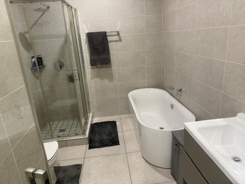 Modern bathroom featuring a freestanding bathtub, separate glass-enclosed shower, and a vanity unit with neutral floor-to-ceiling tiling.