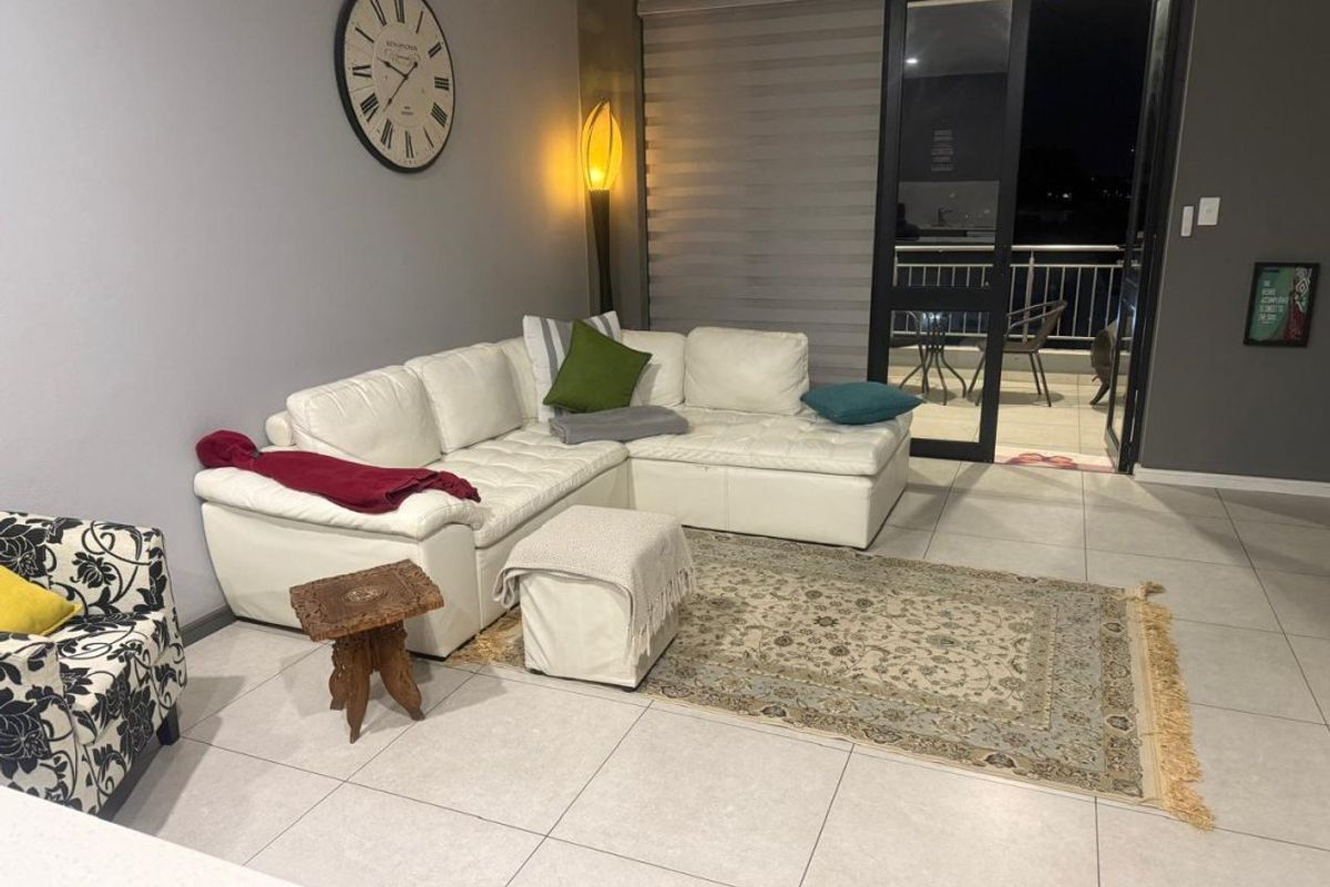 A well-lit living room featuring large format floor tiles and direct access to an outdoor balcony through a sliding glass door.