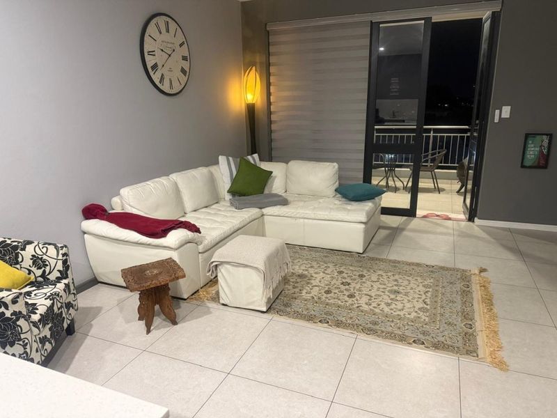 A well-lit living room featuring large format floor tiles and direct access to an outdoor balcony through a sliding glass door.