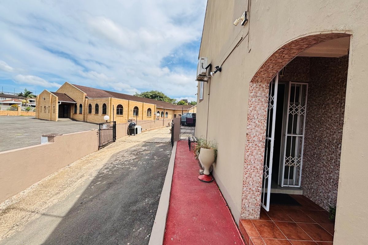 Side exterior view showing a paved driveway, security gate, and a tiled entrance area with an external air conditioning unit.