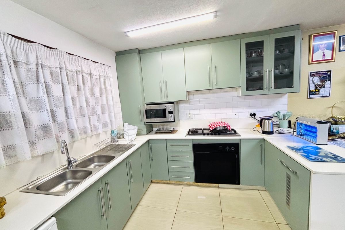 A functional kitchen featuring sage green cabinetry, a subway tile backsplash, built-in oven, gas hob, and a double basin sink with tiled flooring.
