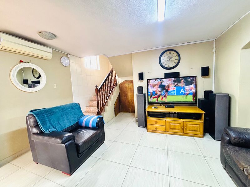 A living room featuring tiled flooring, a staircase with a wooden banister, and a wall-mounted air conditioning unit.